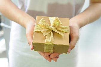 Hands holding a gold gift box with a shiny bow