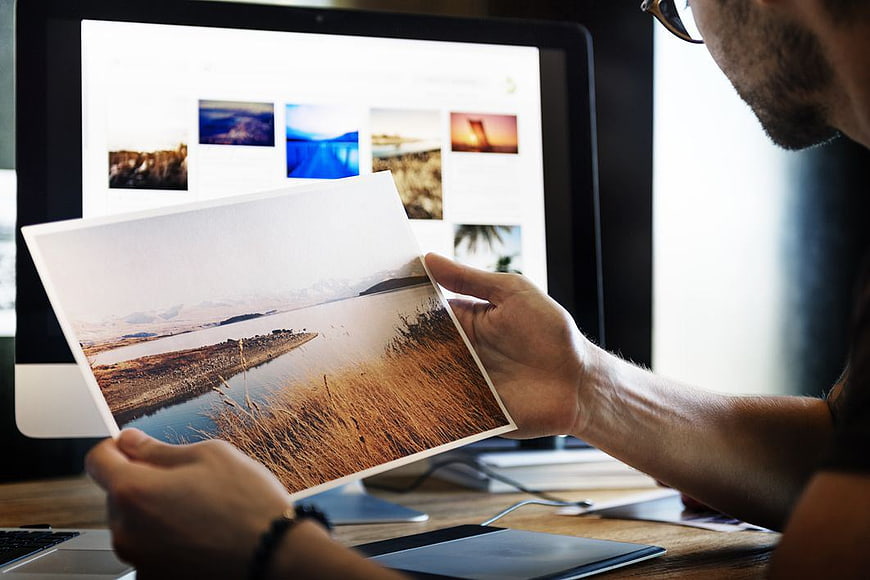 Photographer comparing printed landscape photo with digital screen