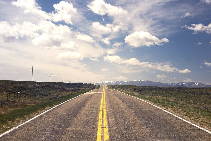 Straight Highway Stretching to Snow-Capped Mountains Under Blue Sky