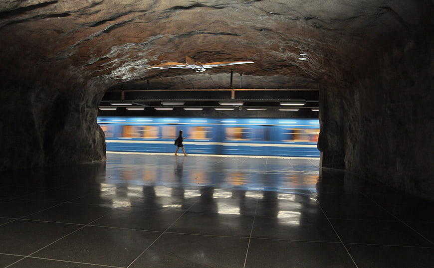 Blue subway train blurring through a cavernous underground station