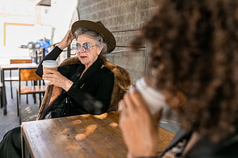 Senior woman in hat and sunglasses drinking coffee at cafe