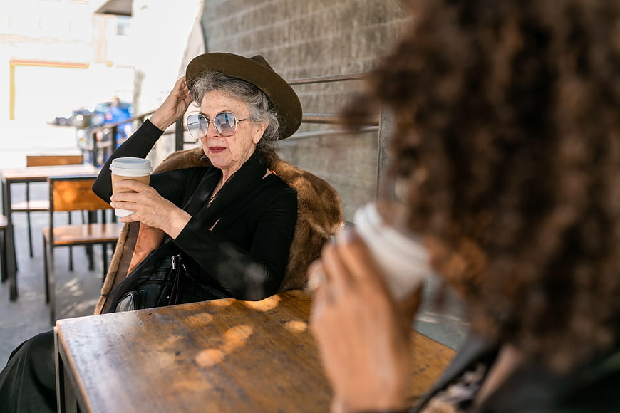 Senior woman in hat and sunglasses drinking coffee at cafe