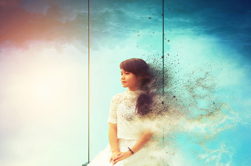 Woman dissolving into particles against blue sky background