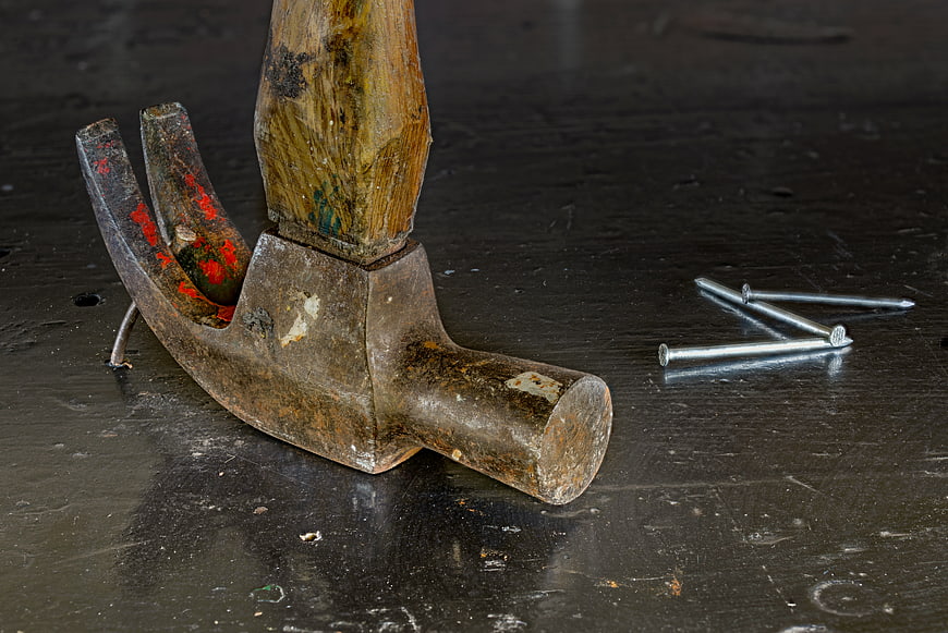 Old rusty claw hammer and nails on dark workbench