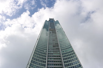 Low angle view of modern glass skyscraper against cloudy sky