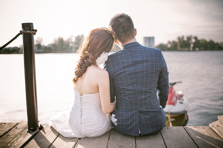 Bride and groom sitting on wooden dock by lake