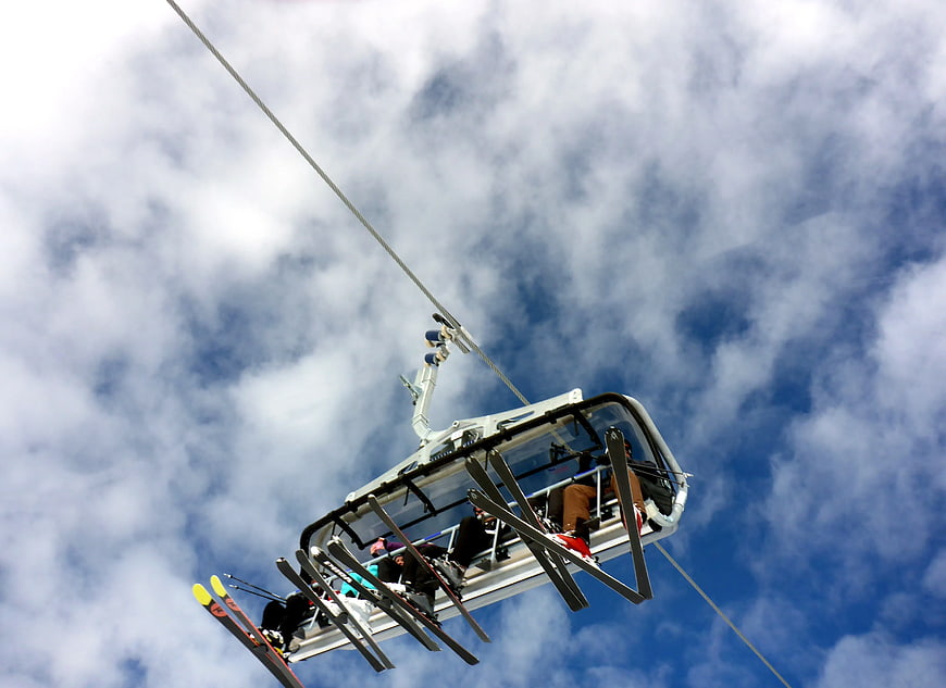 Low angle view of skiers on a chairlift against blue sky