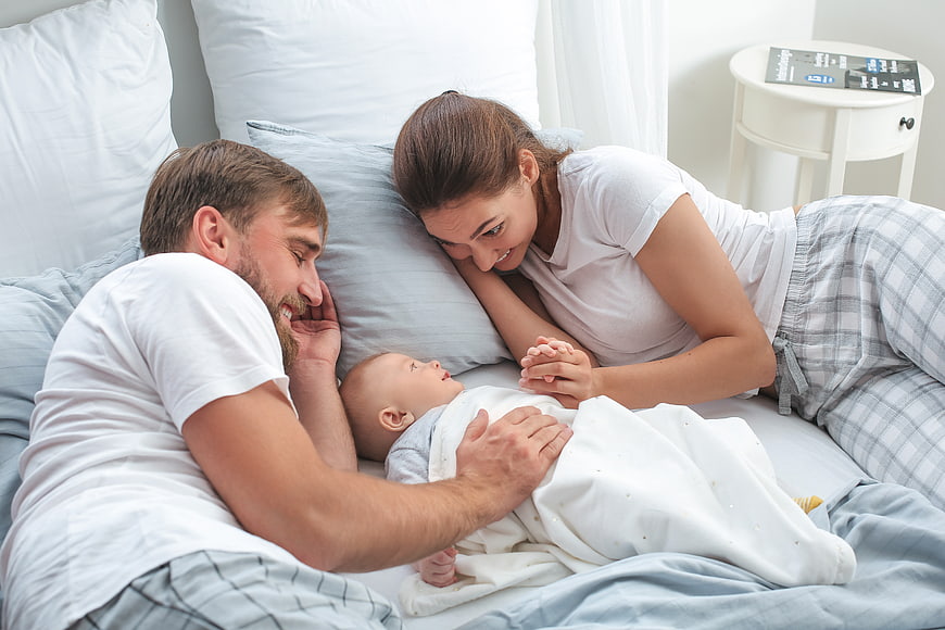 Happy Parents Lying in Bed with Newborn Baby