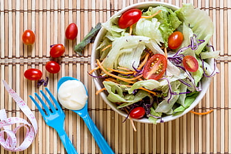 Healthy salad bowl with measuring tape and dressing on bamboo mat
