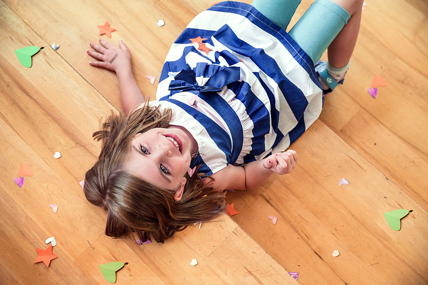 Happy Girl Lying on Wooden Floor with Confetti