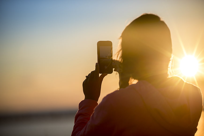 Woman Taking Photo of Sunset with Smartphone Silhouette
