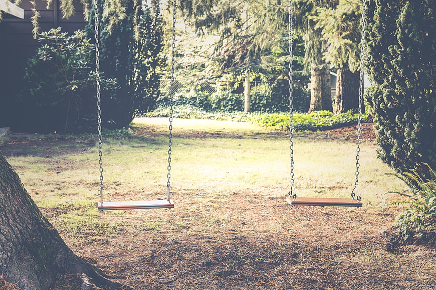 Empty wooden swings in a sunny backyard with trees