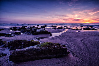 Dramatic Sunset Over Rocky Beach with Purple Sky