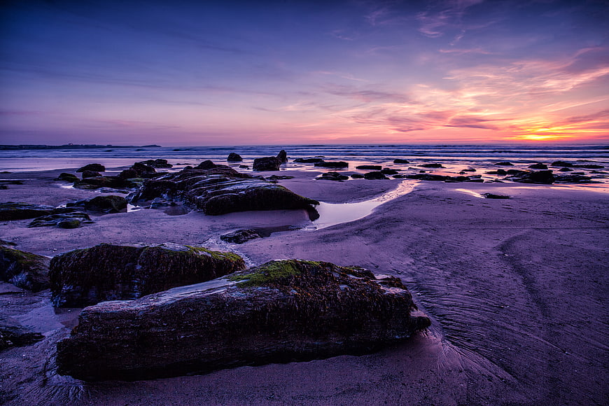 Dramatic Sunset Over Rocky Beach with Purple Sky