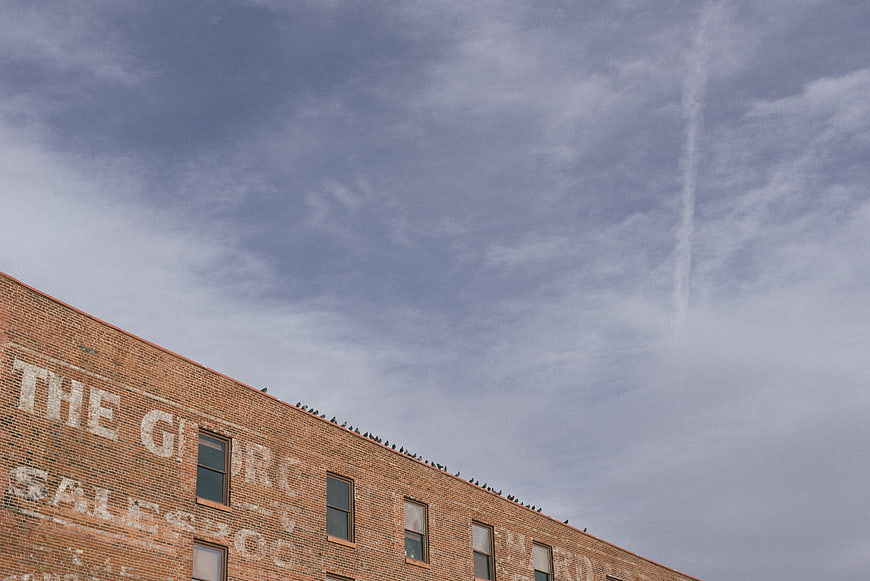 Low angle view of brick building with faded ghost sign and pigeons