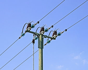 Wooden utility pole with high voltage insulators against clear blue sky