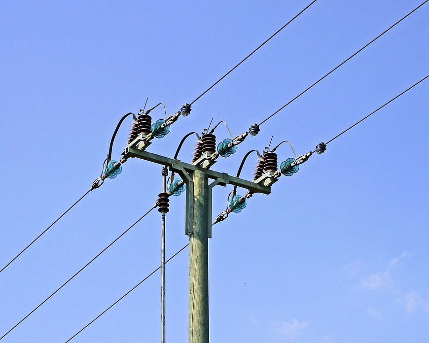 Wooden utility pole with high voltage insulators against clear blue sky