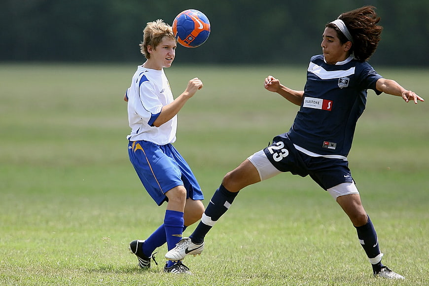 Two teenage boys competing for a soccer ball on a grass field