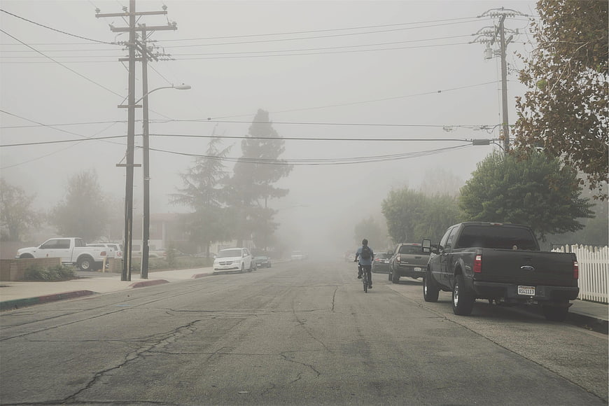 Cyclist riding down foggy suburban street with parked trucks