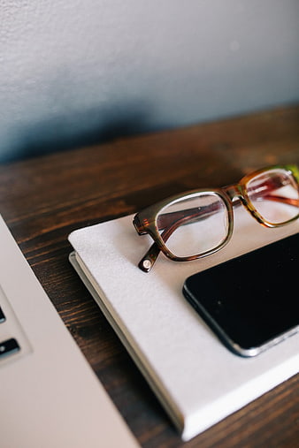 Close-up of eyeglasses, smartphone, and notebook on wooden desk