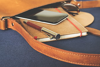 Leather bag with notebook, smartphone, and pen on blue fabric
