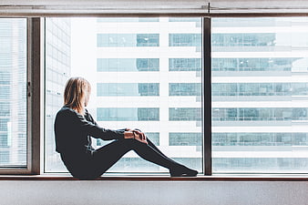 Woman sitting on window sill looking at city building