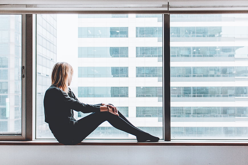 Woman sitting on window sill looking at city building