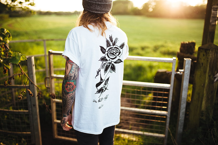 Person with tattoos wearing rose t-shirt at field gate