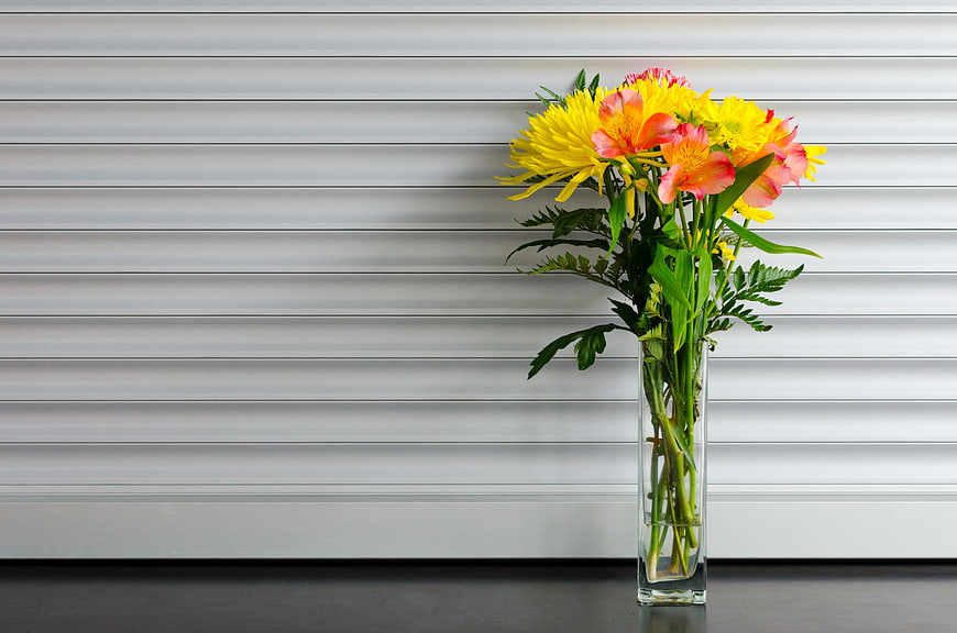 Yellow and Pink Flowers in Glass Vase Against White Blinds