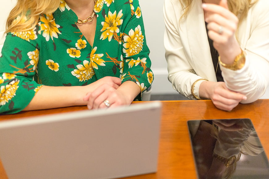 Two female professionals collaborating at a desk with laptop and tablet