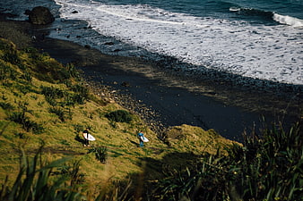 Surfers walking down grassy cliff to black sand beach