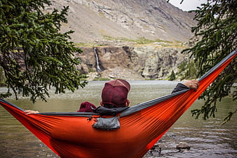 Man relaxing in orange hammock by mountain lake