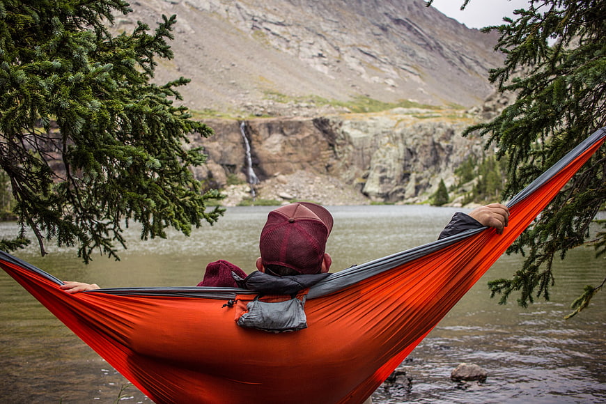 Man relaxing in orange hammock by mountain lake