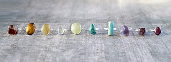 Row of colorful gemstone rings on gray textured surface