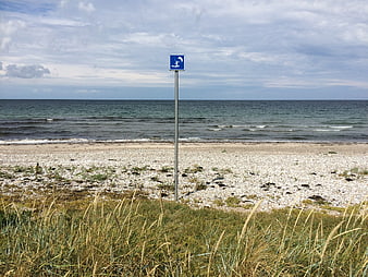 Blue windsurfing sign on a pebble beach with sea and dune grass