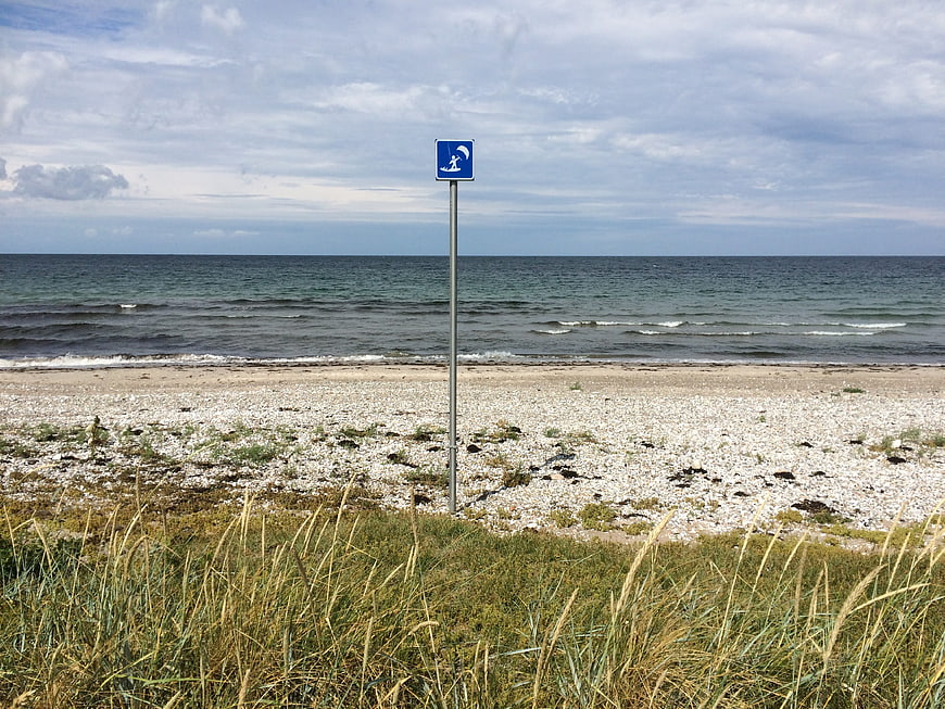 Blue windsurfing sign on a pebble beach with sea and dune grass