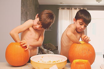 Two shirtless boys carving pumpkins for Halloween