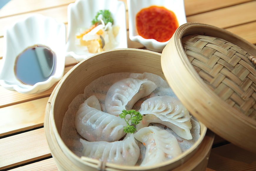 Steamed dumplings in bamboo steamer with soy sauce and chili