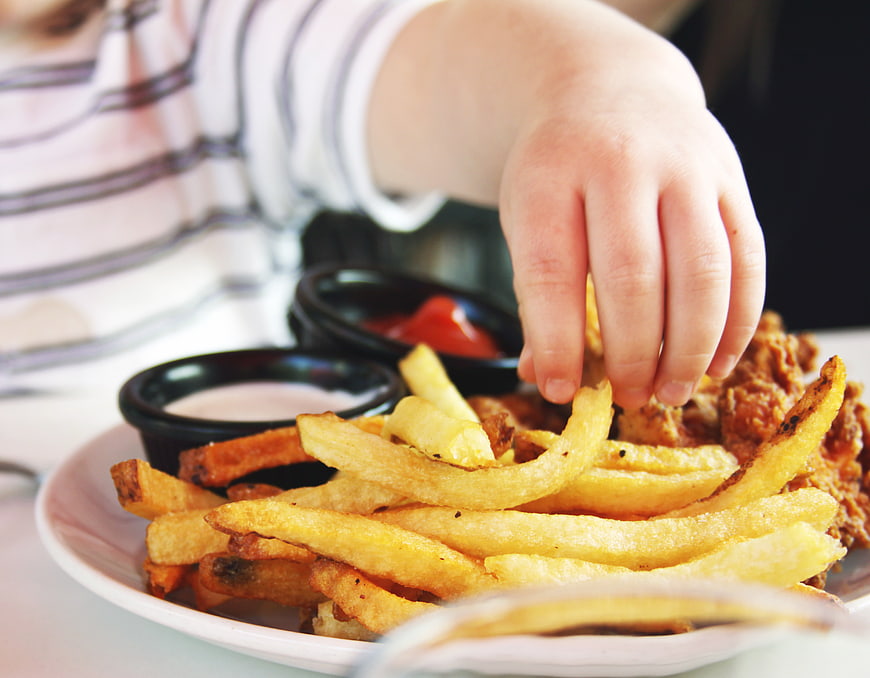 Child's Hand Reaching for French Fries and Fried Chicken