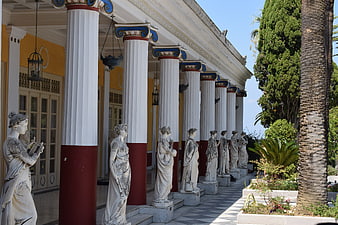 Classical statues lining a colonnade with white columns and garden