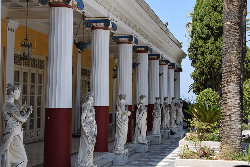 Classical statues lining a colonnade with white columns and garden