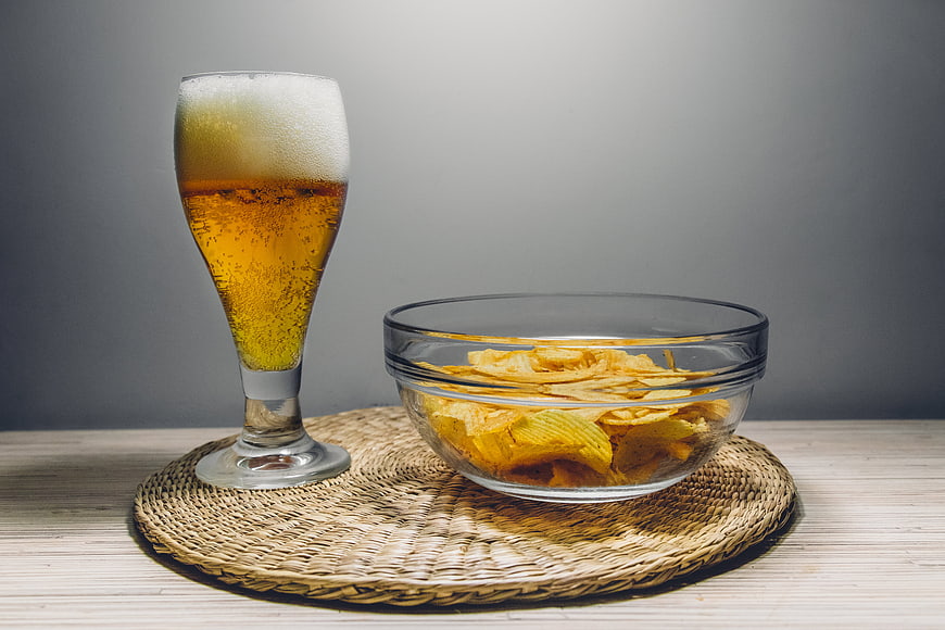 Glass of beer and bowl of potato chips on woven mat