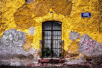 Textured yellow wall with barred window and street sign
