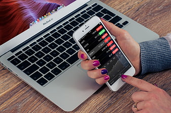 Woman checking stock market app on smartphone with laptop