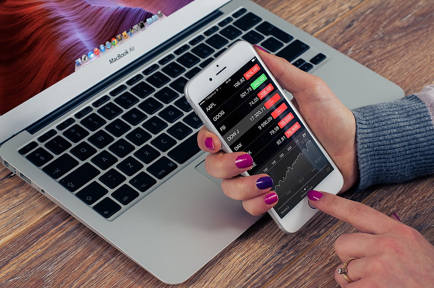 Woman checking stock market app on smartphone with laptop