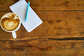 Flat lay of cappuccino, notebook, and pen on rustic wood