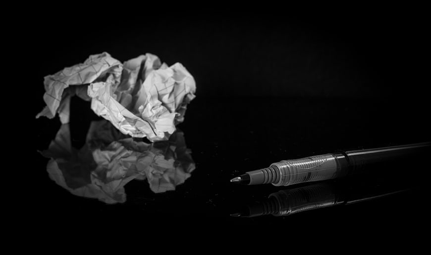 Crumpled paper ball and pen on reflective black surface