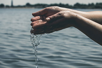 Close-up of hands pouring water over a lake background