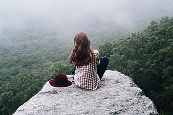 Woman sitting on a rocky cliff overlooking a misty green forest