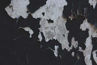 Close-up of peeling black paint on a textured concrete wall
